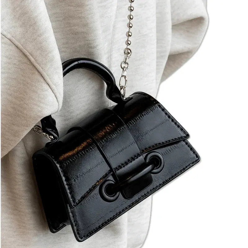 Mini sac noir brillant porté en bandoulière avec chaîne fine.