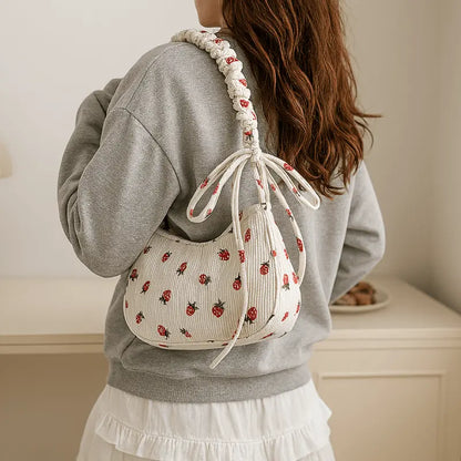 porte.jpg	Petit sac en velours côtelé écru à motifs fraises porté à l’épaule par une femme.